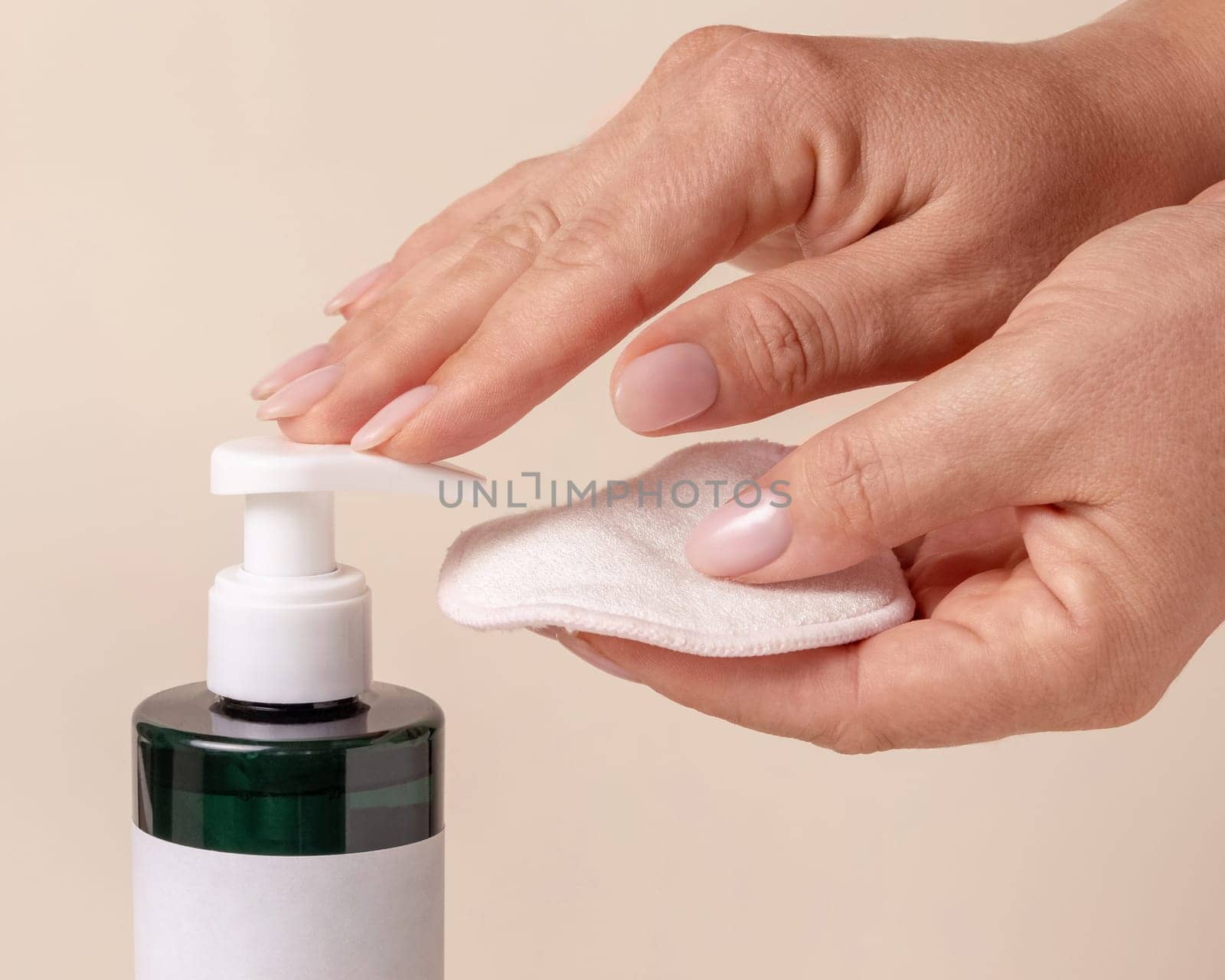 A woman hand pumping liquid on a make-up remover pad from a cosmetic bottle on beige close up. Skincare beauty product package, minimal composition..