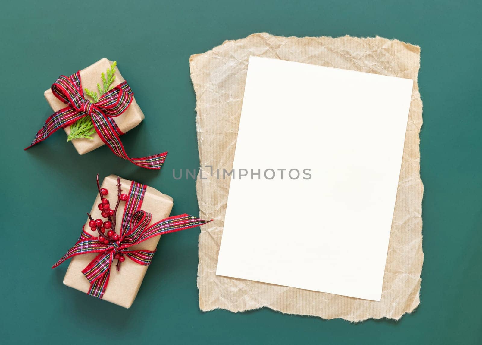 Blank paper card and wrapped Christmas presents on a green background top view. Holidays winter mockup, copy space. New Year and Christmas holiday atmospheric flat lay