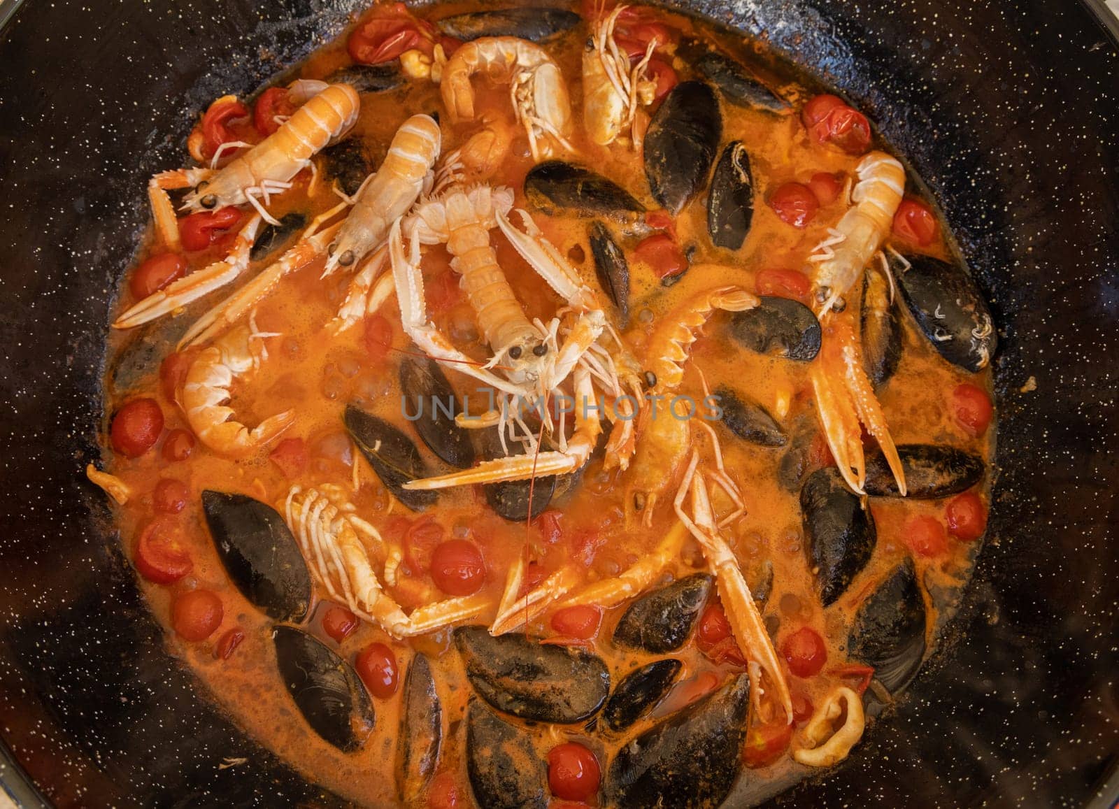 Cooking Italian stew with seafood and tomatoes in a big frying pan top view. Mediterranean Apulian traditional food with fresh stewed clams, shrimps, mussels, octopus and squid