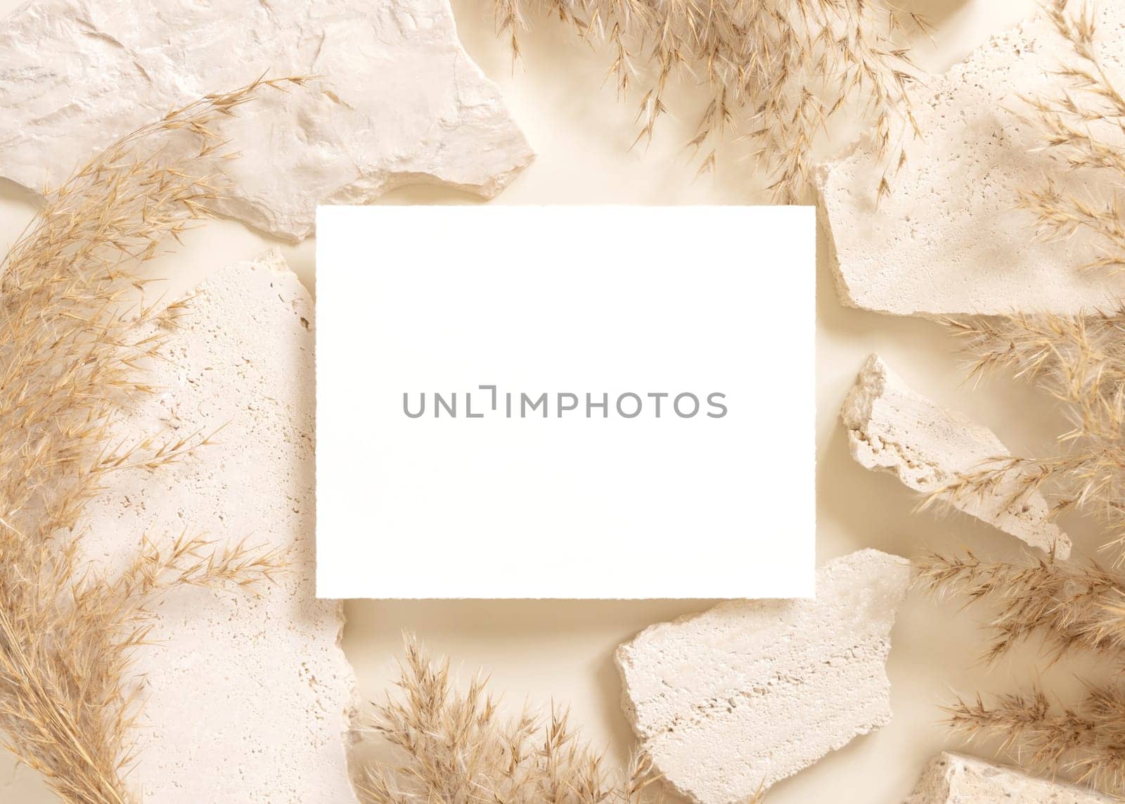 Blank card near beige travertine stones and dried pampas grass top view, mockup. Boho scene with horizontal card. Bohemian or close to nature greeting or wedding Invitation. Close to nature.