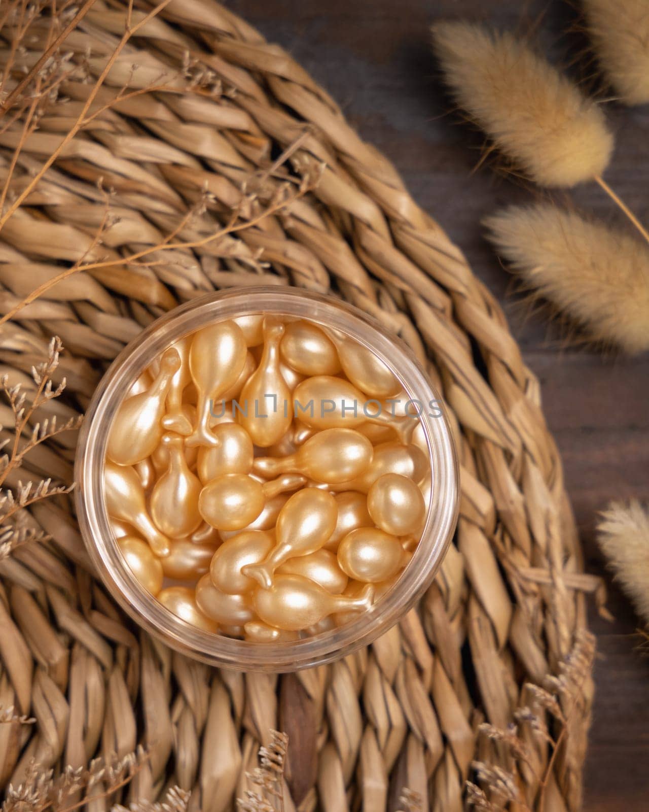 Beauty serum capsules in a jar on wattled boho placemat on wood near Hare's Tail grass top view. Natural skincare product for everyday beauty routine. Bohemian eco friendly cosmetics flat lay.