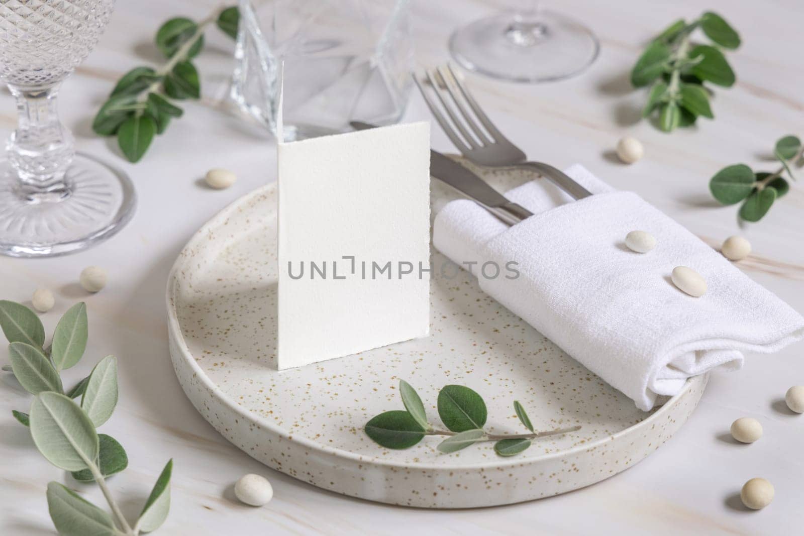 Elegant Table setting with a folded card decorated with eucalyptus branches close up, Wedding Mockup. Romantic table with blank card. Close to nature and simplicity concepts