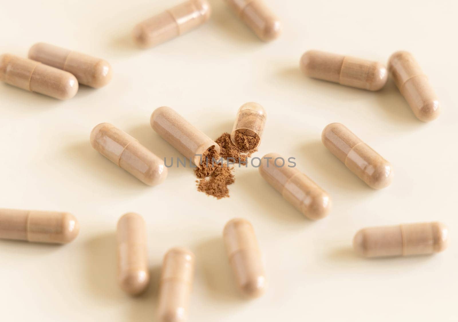 Medical capsules on light beige close up. One capsule opened to show brown powder. Preventive medicine and healthcare, taking dietary supplements and vitamins. Pharmaceutical product