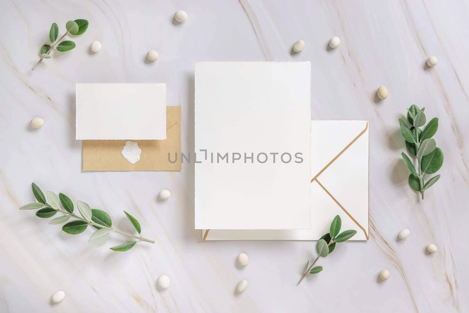 Cards and envelope on a marble table near eucalyptus branches and pebbles top view, Mockup. Romantic flat lay with wedding stationery set. Minimal composition. Close to nature