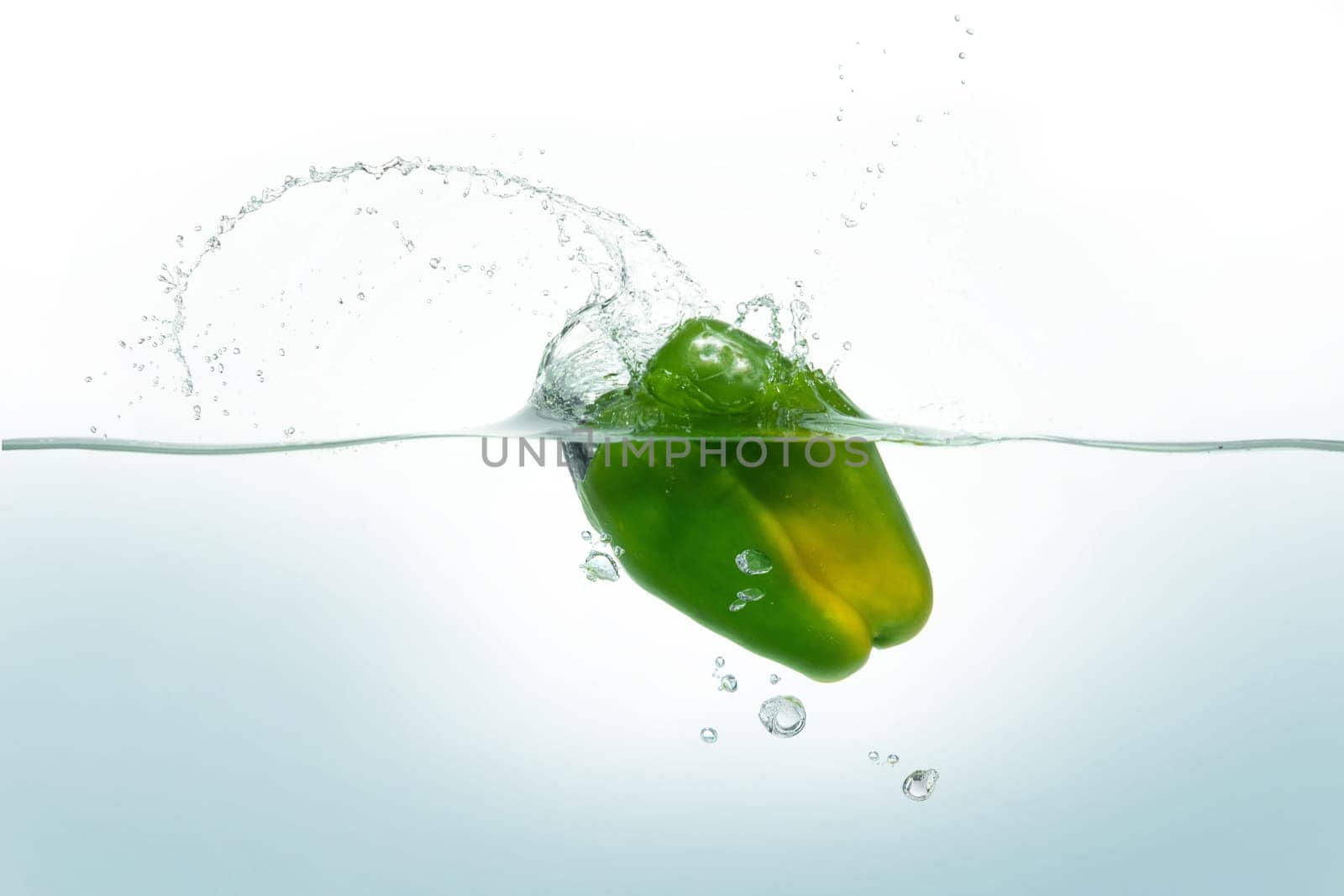 Green pepper splashing in water. Side view on white background.