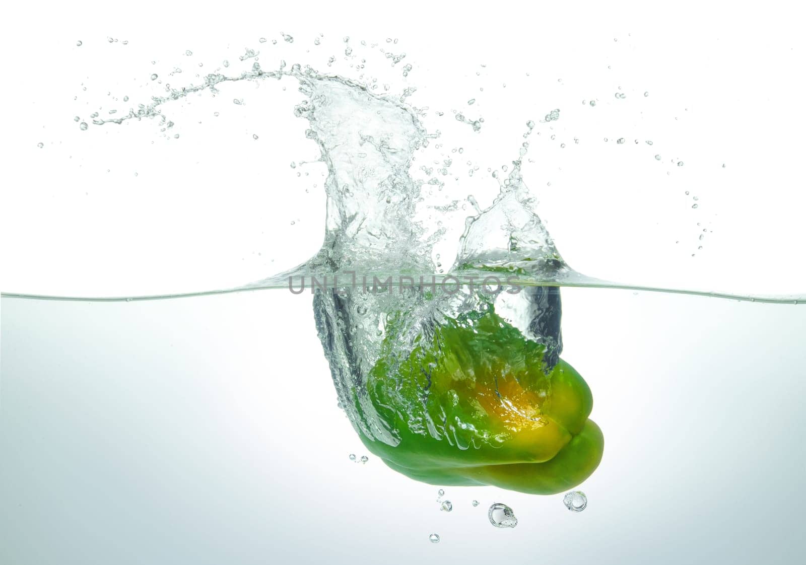 Green pepper splashing in water. Side view on white background.
