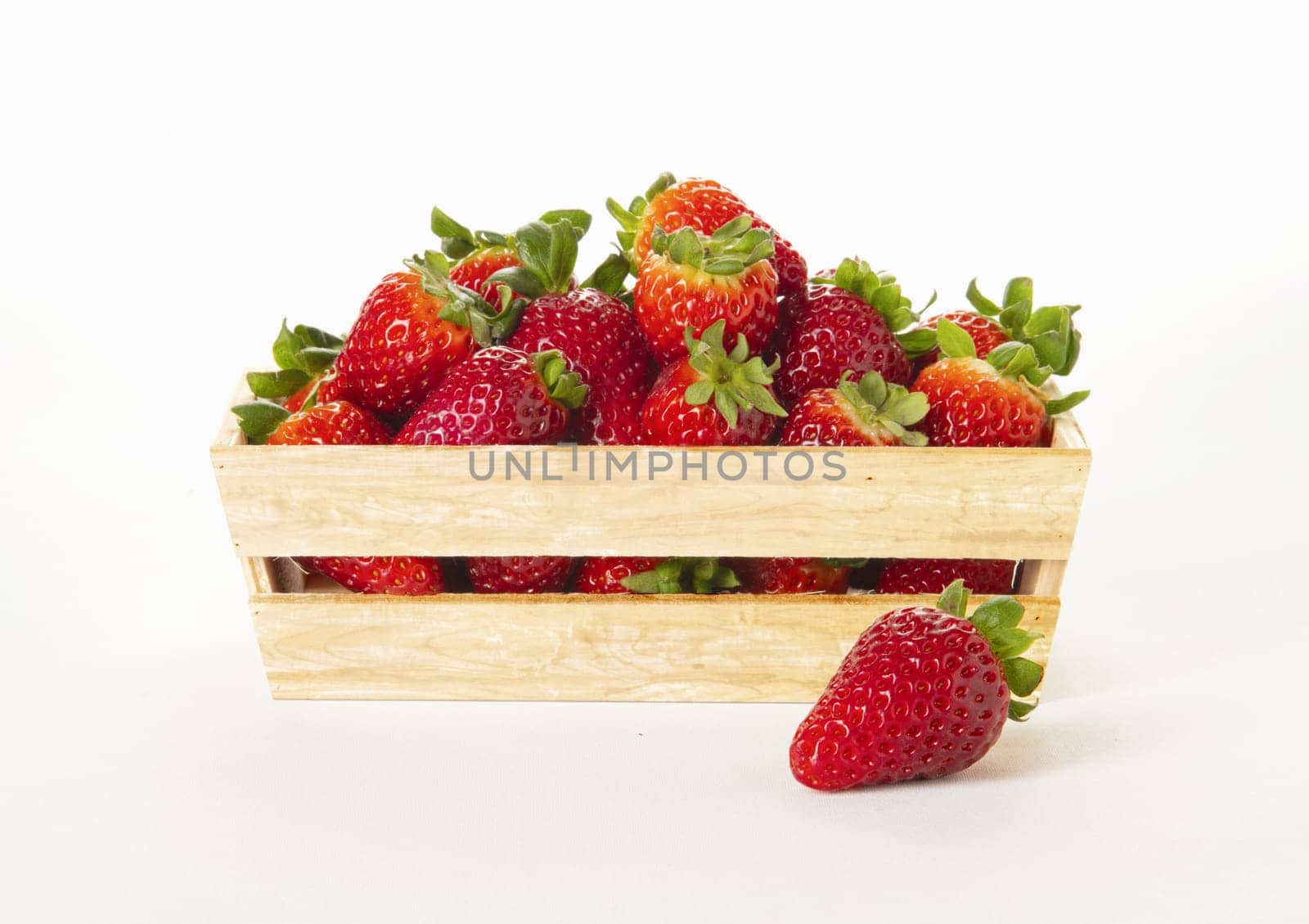 Wooden basket full of strawberries with one out on the surface. On White background.