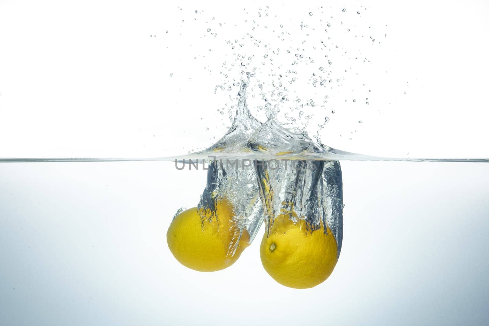 Two lemons splashing in clear water. Side view on white background.