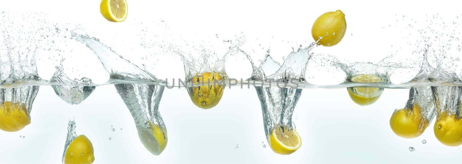 Many lemons splashing in water. Side panoramic view on white background.