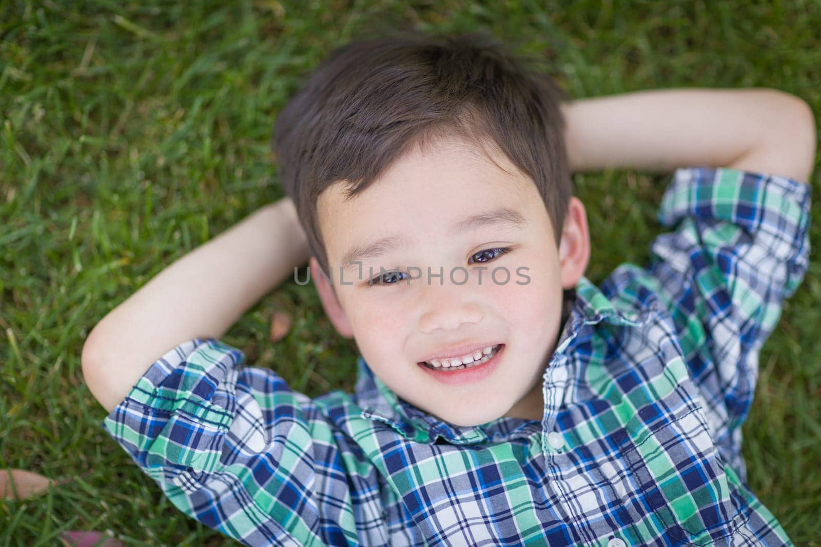 Thoughtful Mixed Race Chinese and Caucasian Young Boy Relaxing On His Back Outside On The Grass