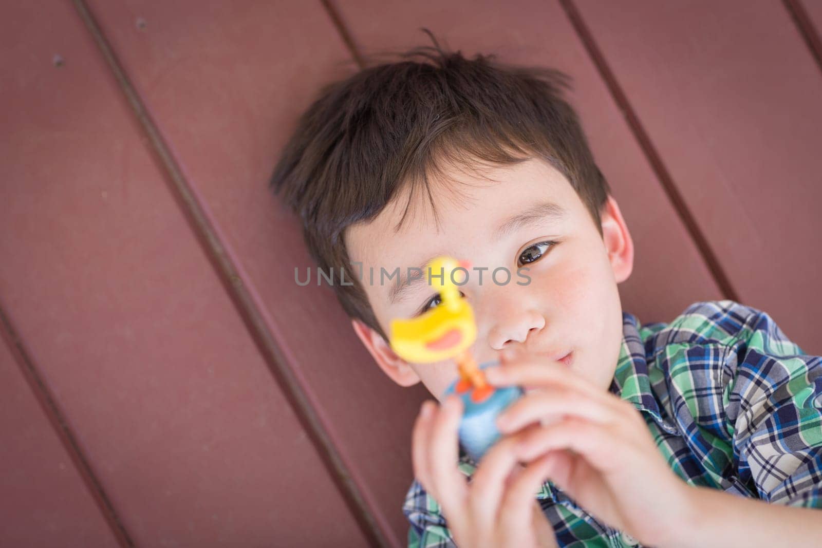 Portrait of Mixed Race Chinese and Caucasian Young Boy Laying On His Porch Playing With Toy