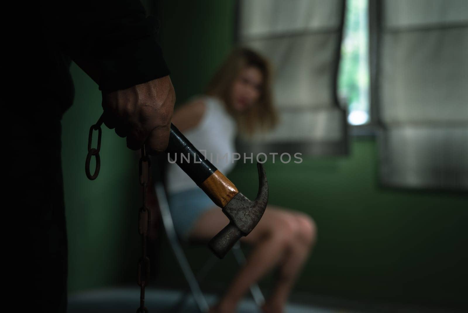 Man hand holding hammer and woman sitting on chair and tied with ropes in dark room
