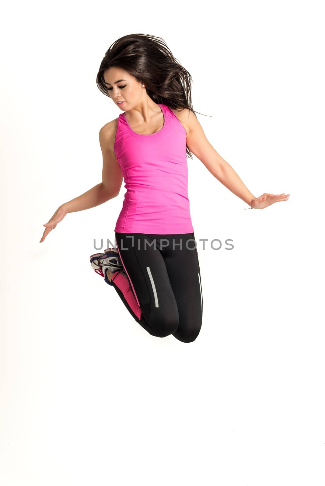 Weight loss fitness woman jumping high, female model isolated on white background in full body. Looking straight with some hair in her face.