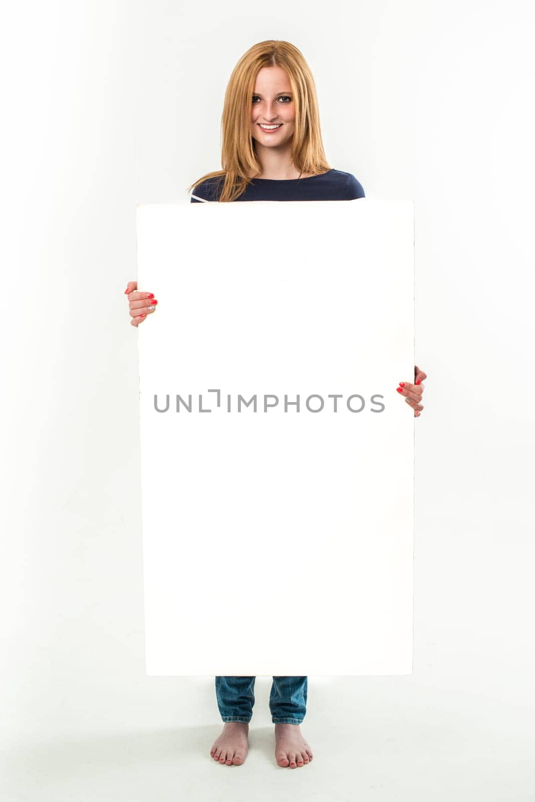 Young blond woman holding a blank banner, standing in jeans and barefoot - isolated over a white background