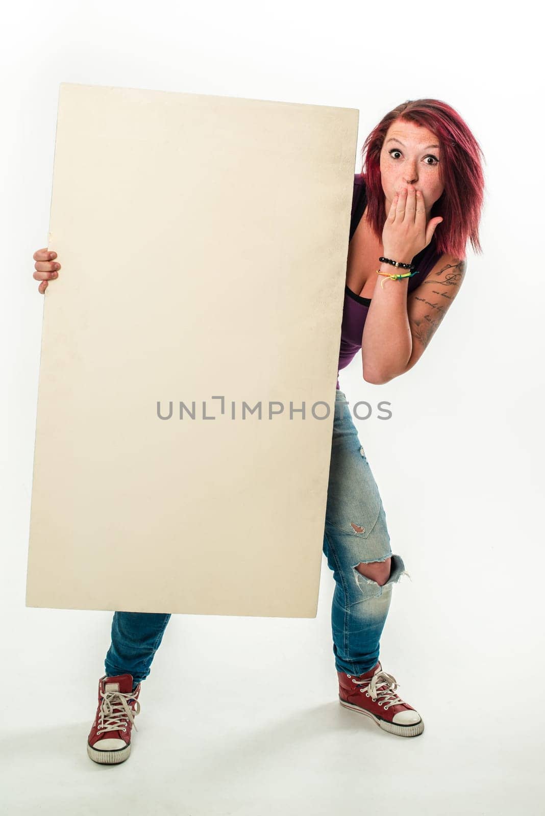 Young red-haired woman holding a blank banner, standing in jeans and red chucks - isolated over a white background