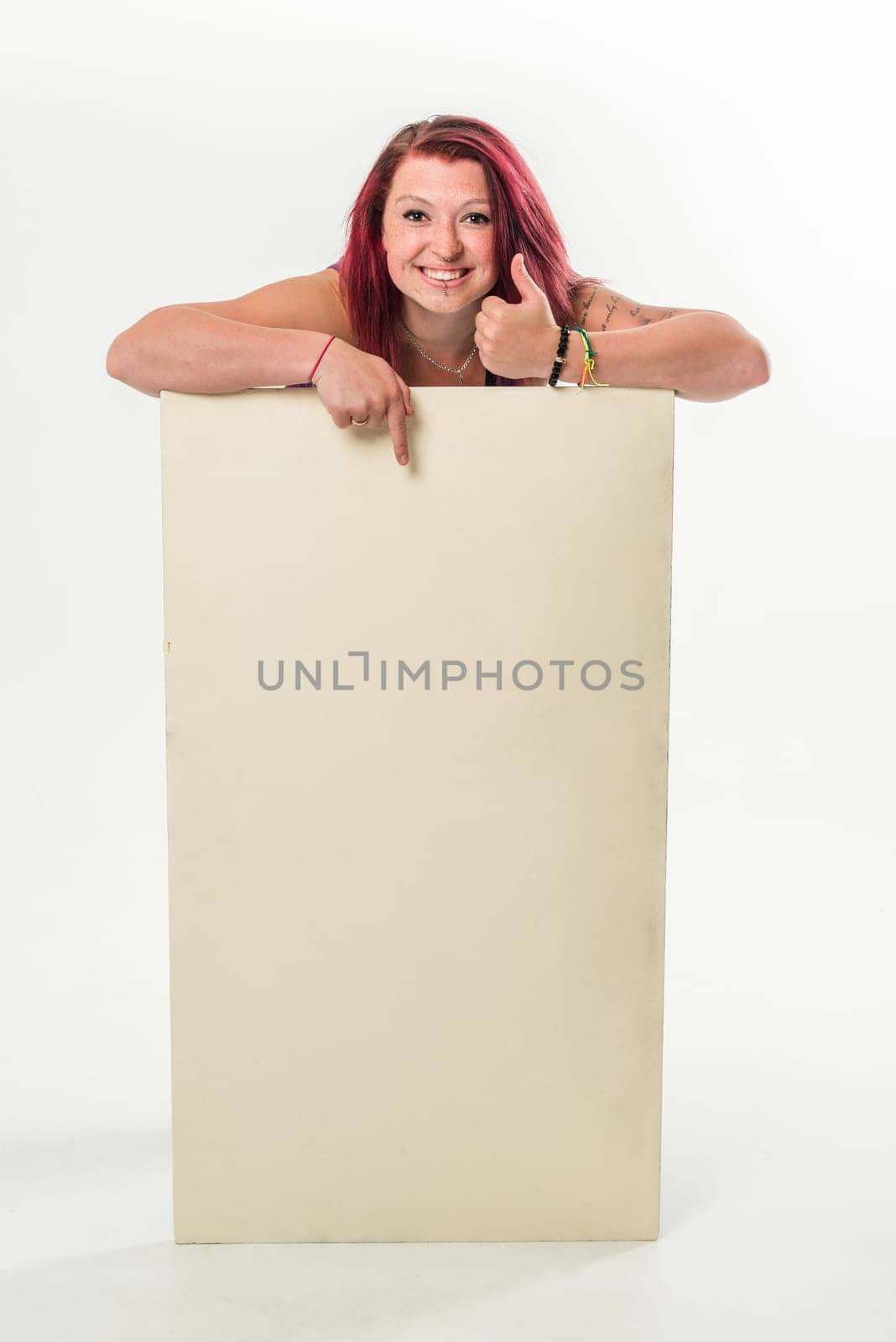 Young red-haired woman holding a blank banner, thumb turned up, top, standing  isolated over a white background