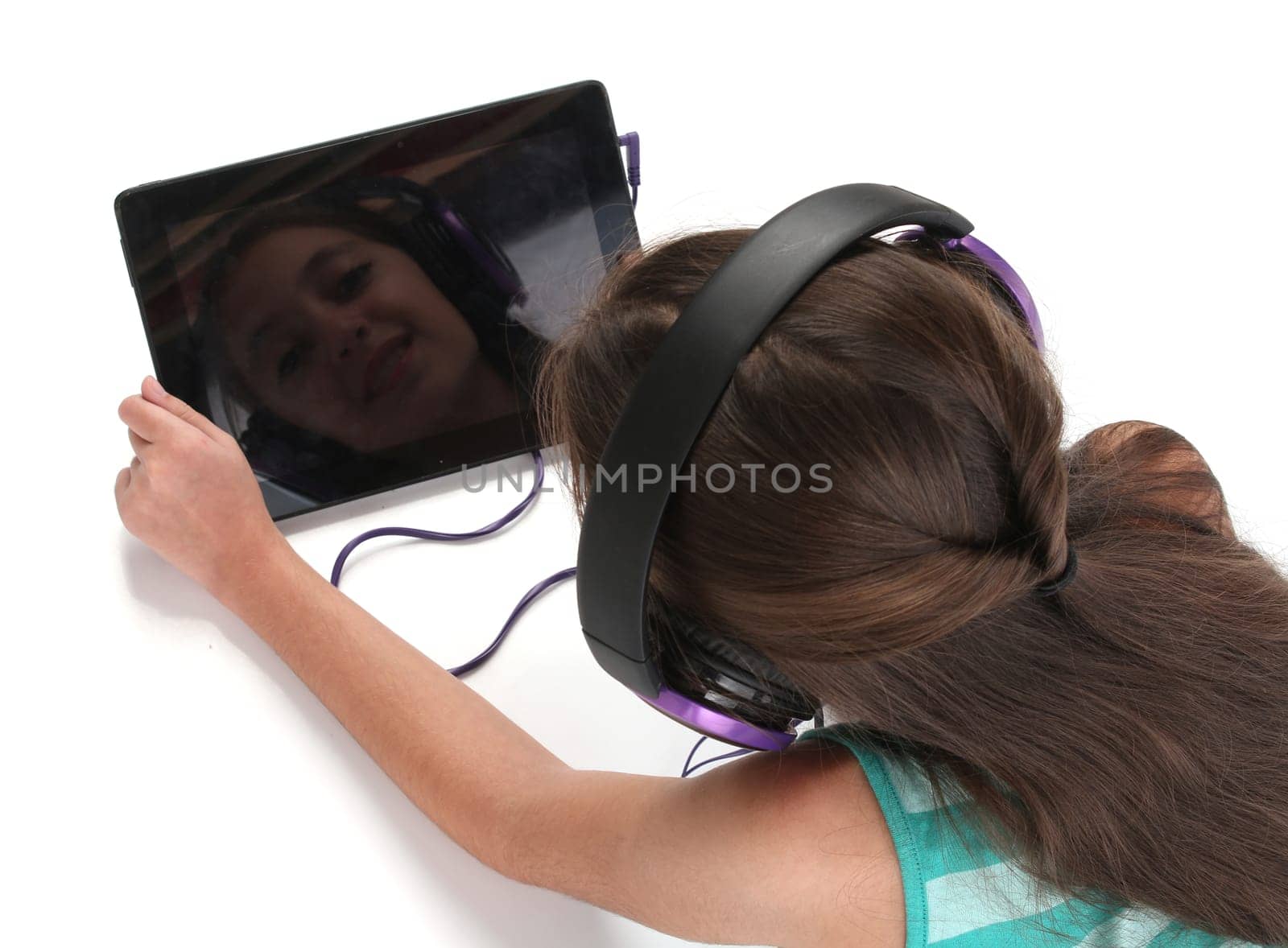 Beautiful pre-teen girl on the floor, usin a tablet computer and headphones, white background