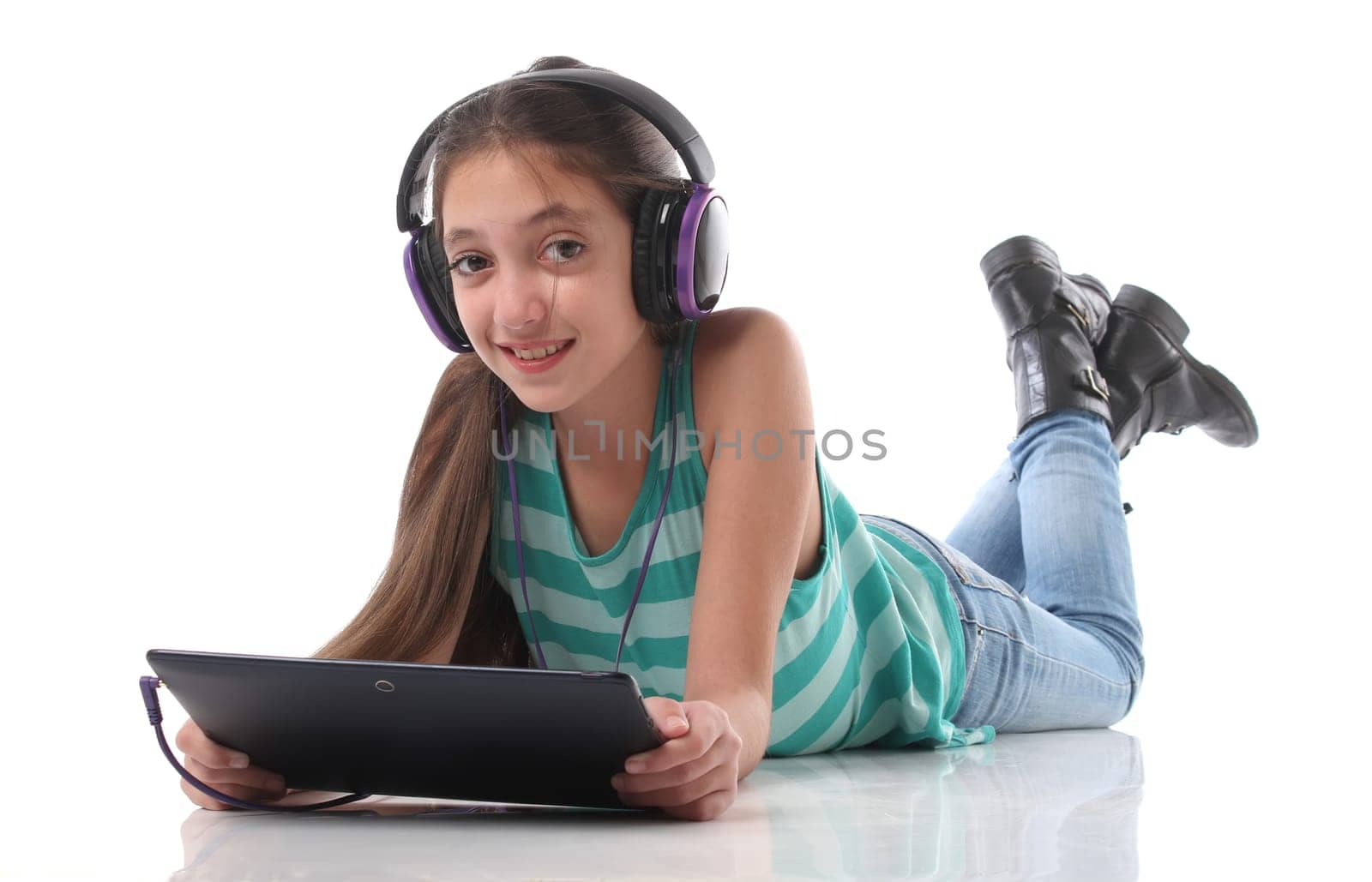 Beautiful pre-teen girl on the floor, usin a tablet computer and headphones, white background