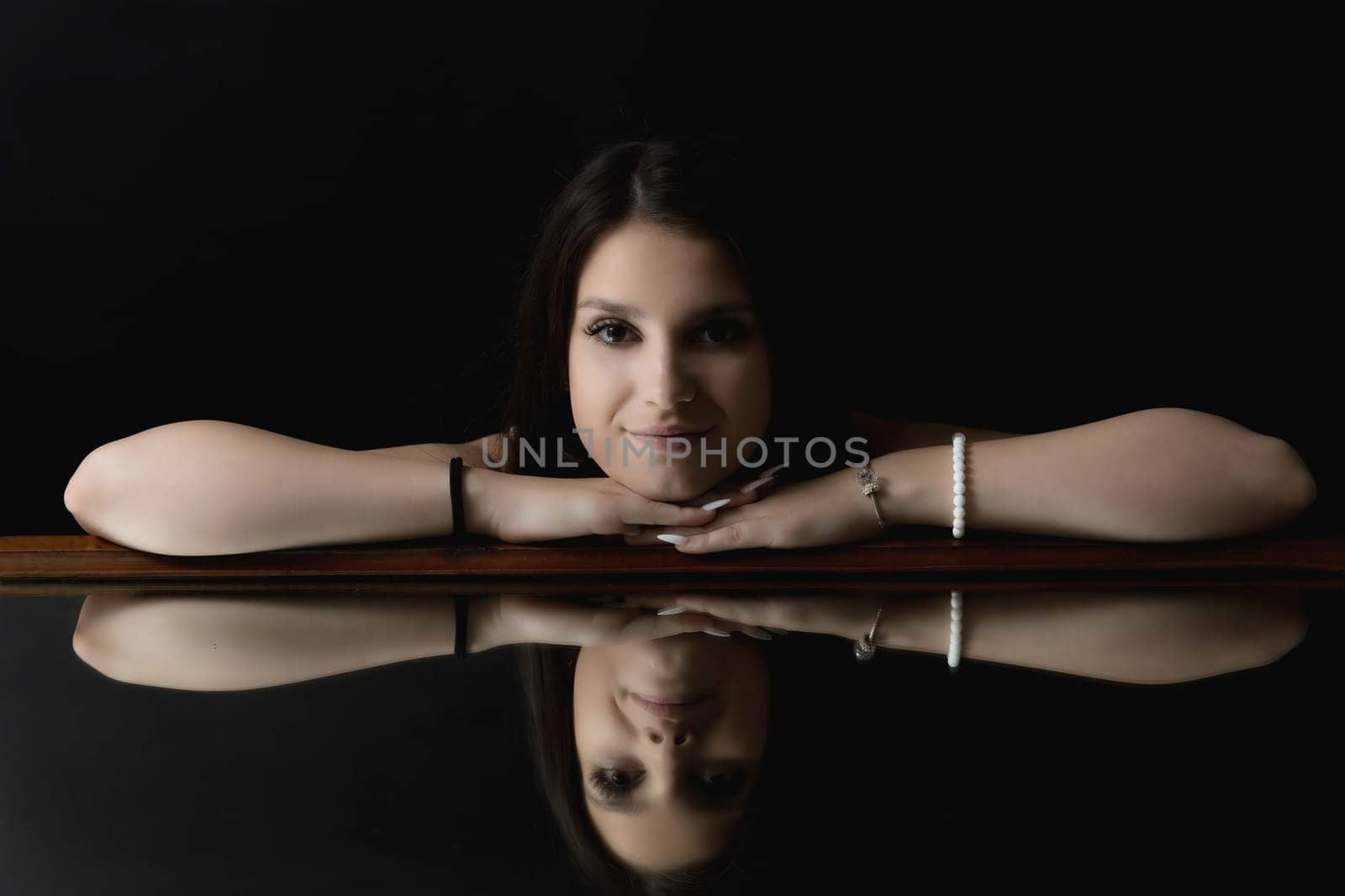Low key portrait of brunette young woman  lying on the mirror. Horizontally.