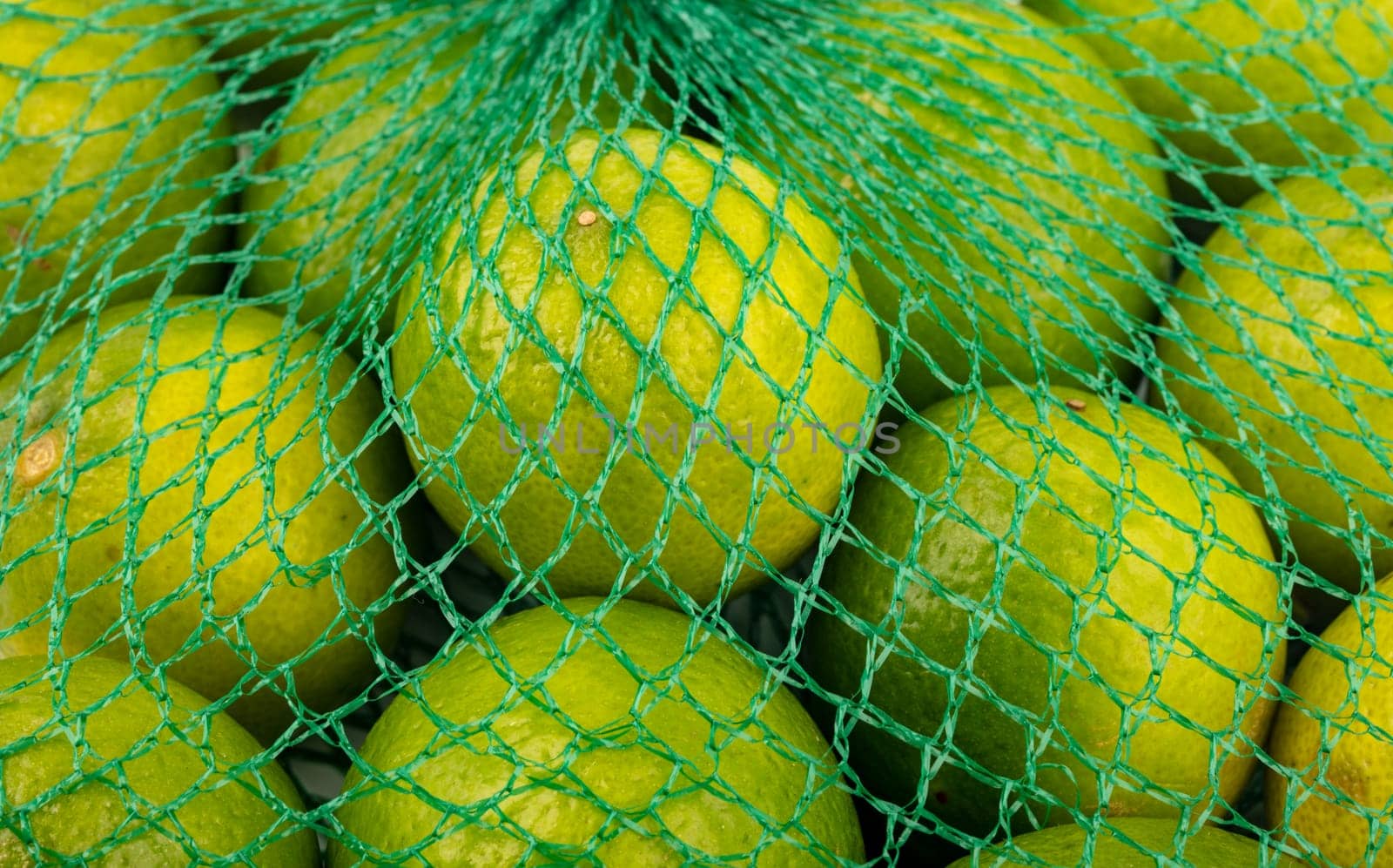 Fresh limes in the net green lime citrus fruit stand fullframe background.