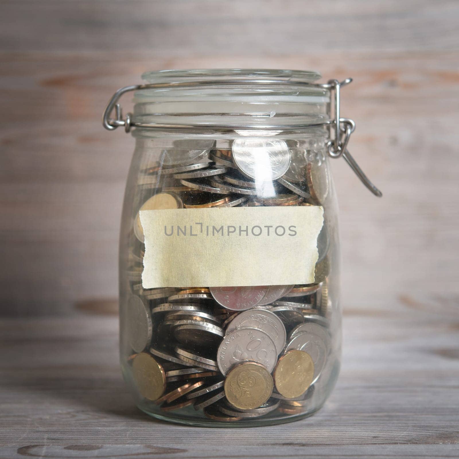 Coins in glass money jar with blank label, financial concept. Vintage wooden background with dramatic light.