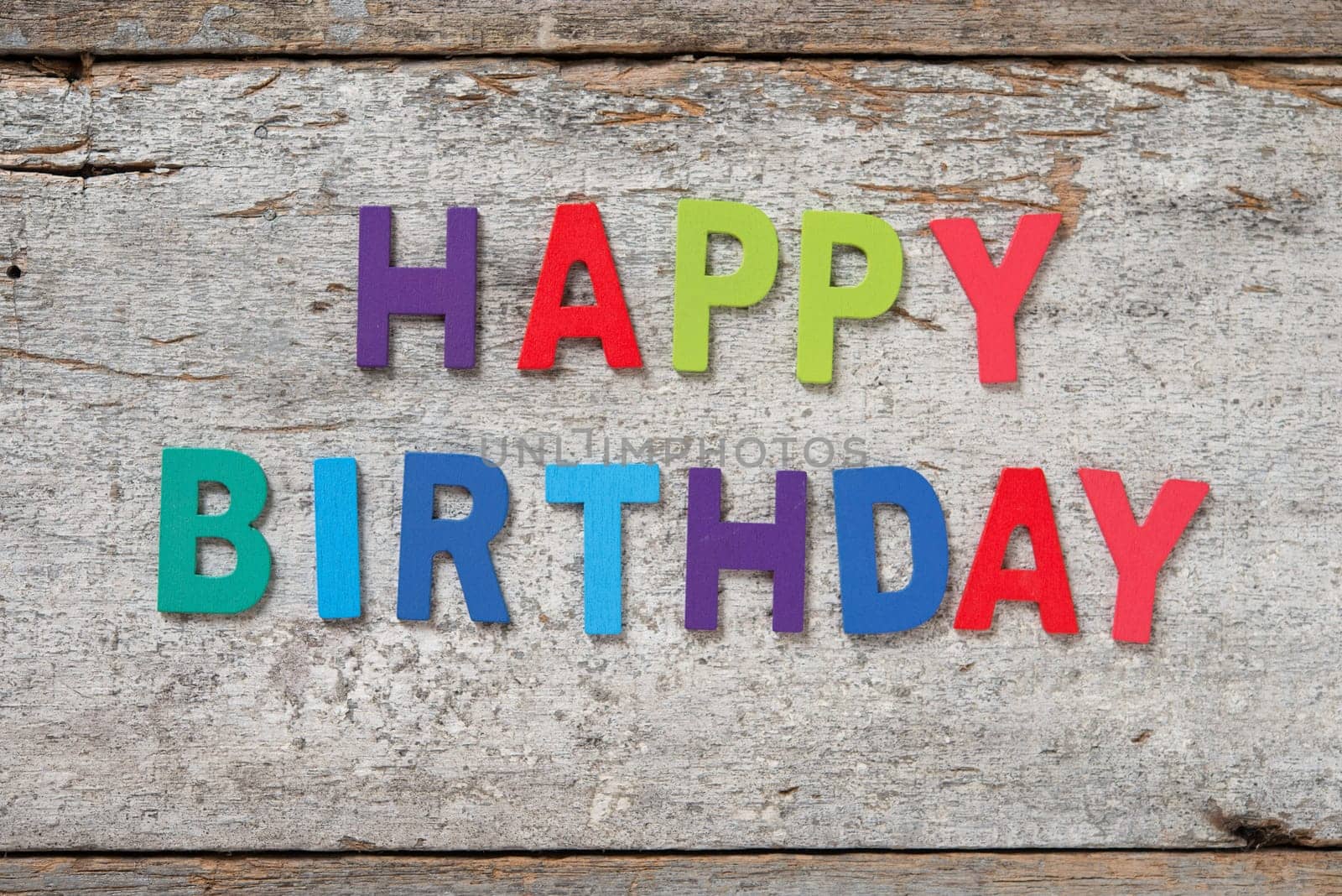 The colorful words "HAPPY BIRTHDAY"" made with wooden letters on old wooden board."