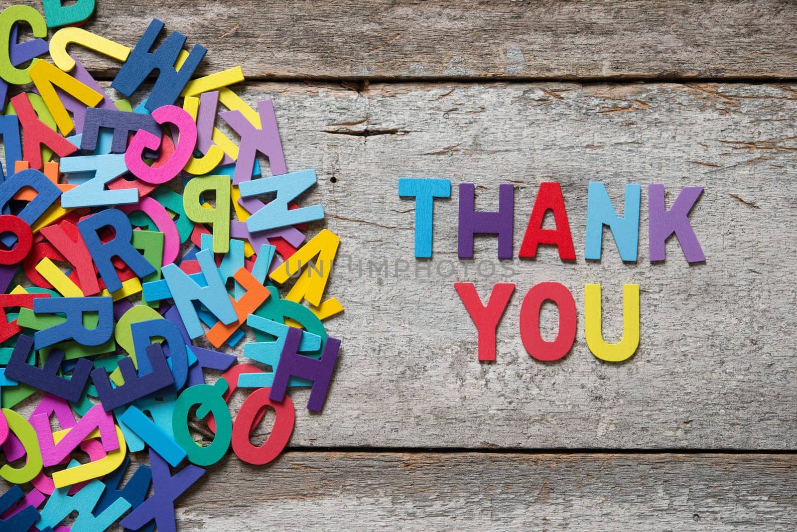 The colorful words "THANK YOU"" made with wooden letters next to a pile of other letters over old wooden board."