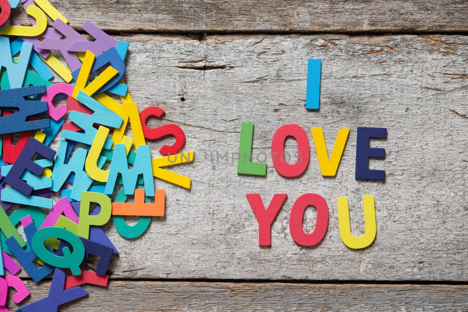 The colorful words "I LOVE YOU"" made with wooden letters next to a pile of other letters over old wooden board."