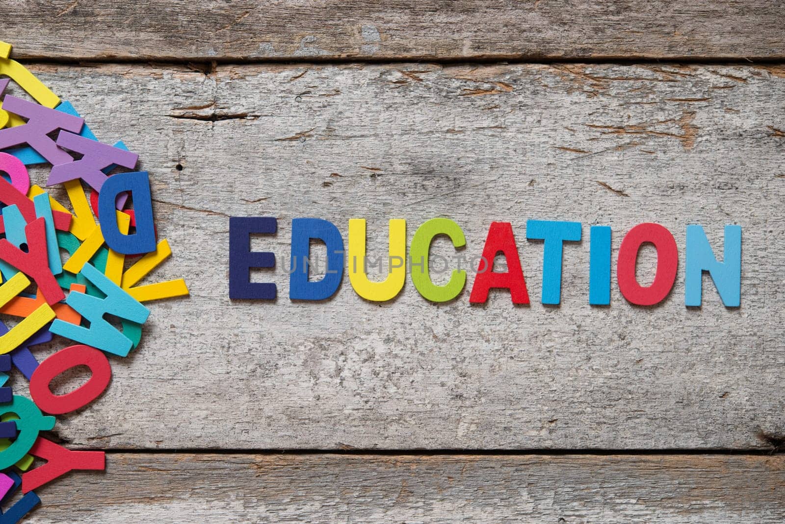 The colorful words "EDUCATION"" made with wooden letters next to a pile of other letters over old wooden board."