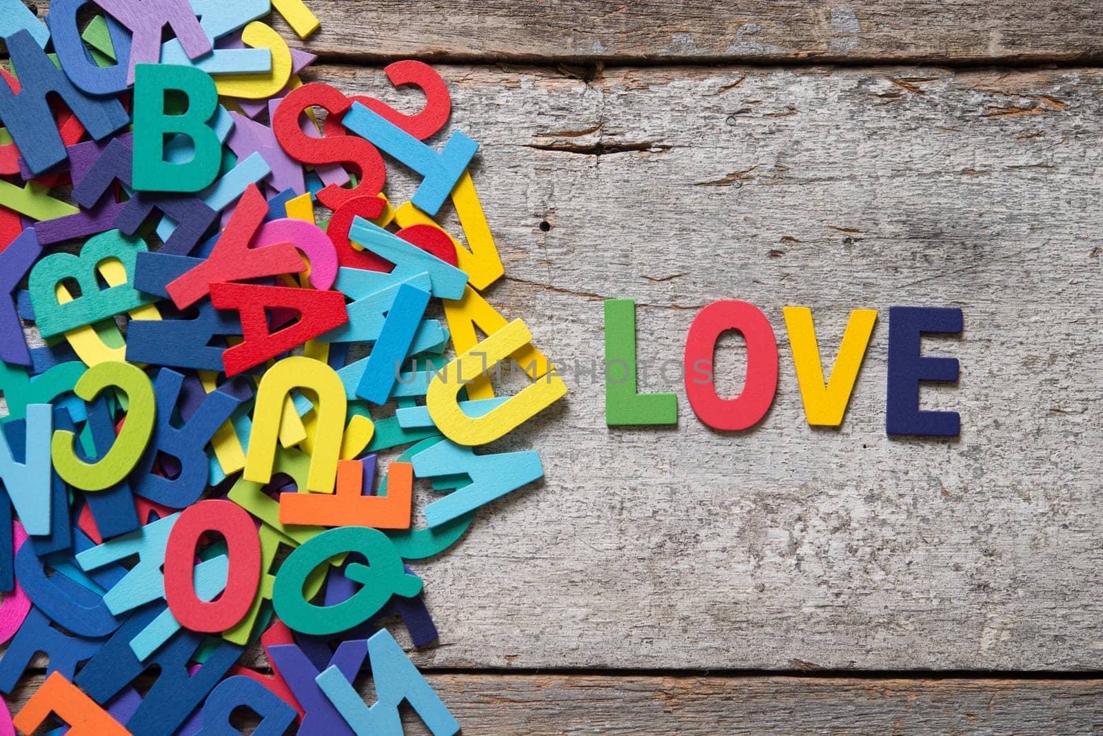 The colorful words "LOVE"" made with wooden letters next to a pile of other letters over old wooden board."