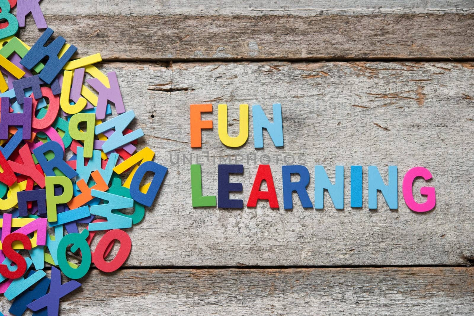 The colorful words "FUN LEANRING"" made with wooden letters next to a pile of other letters over old wooden board."