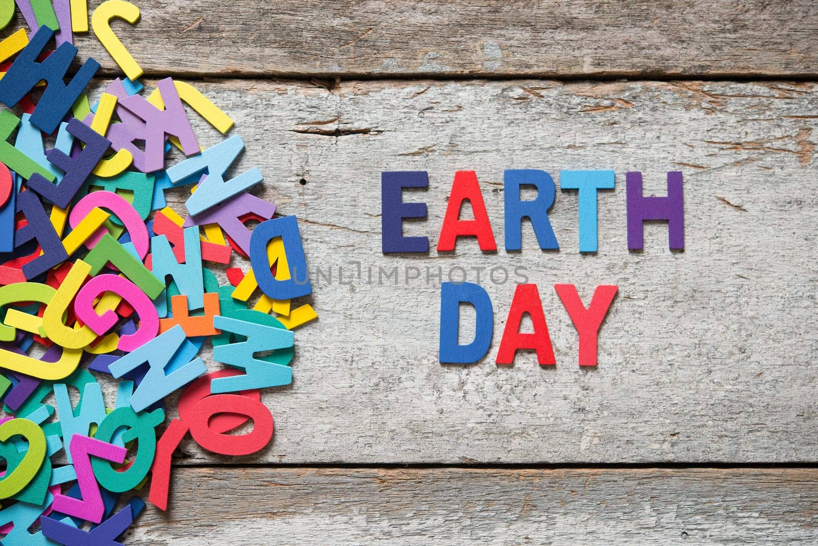The colorful words "EARTH DAY"" made with wooden letters next to a pile of other letters over old wooden board."