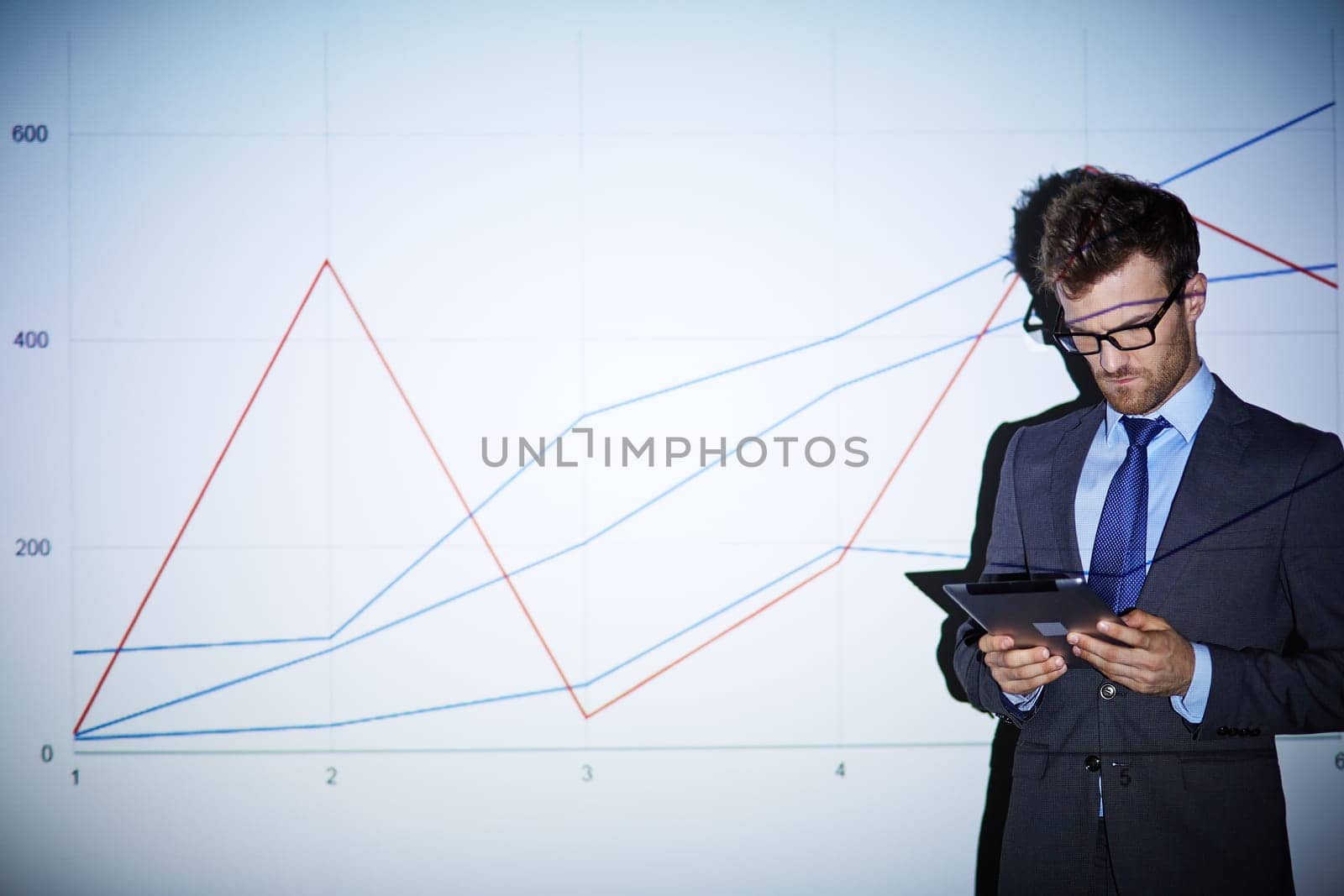 Serious businessman with touchpad standing by wall with graph