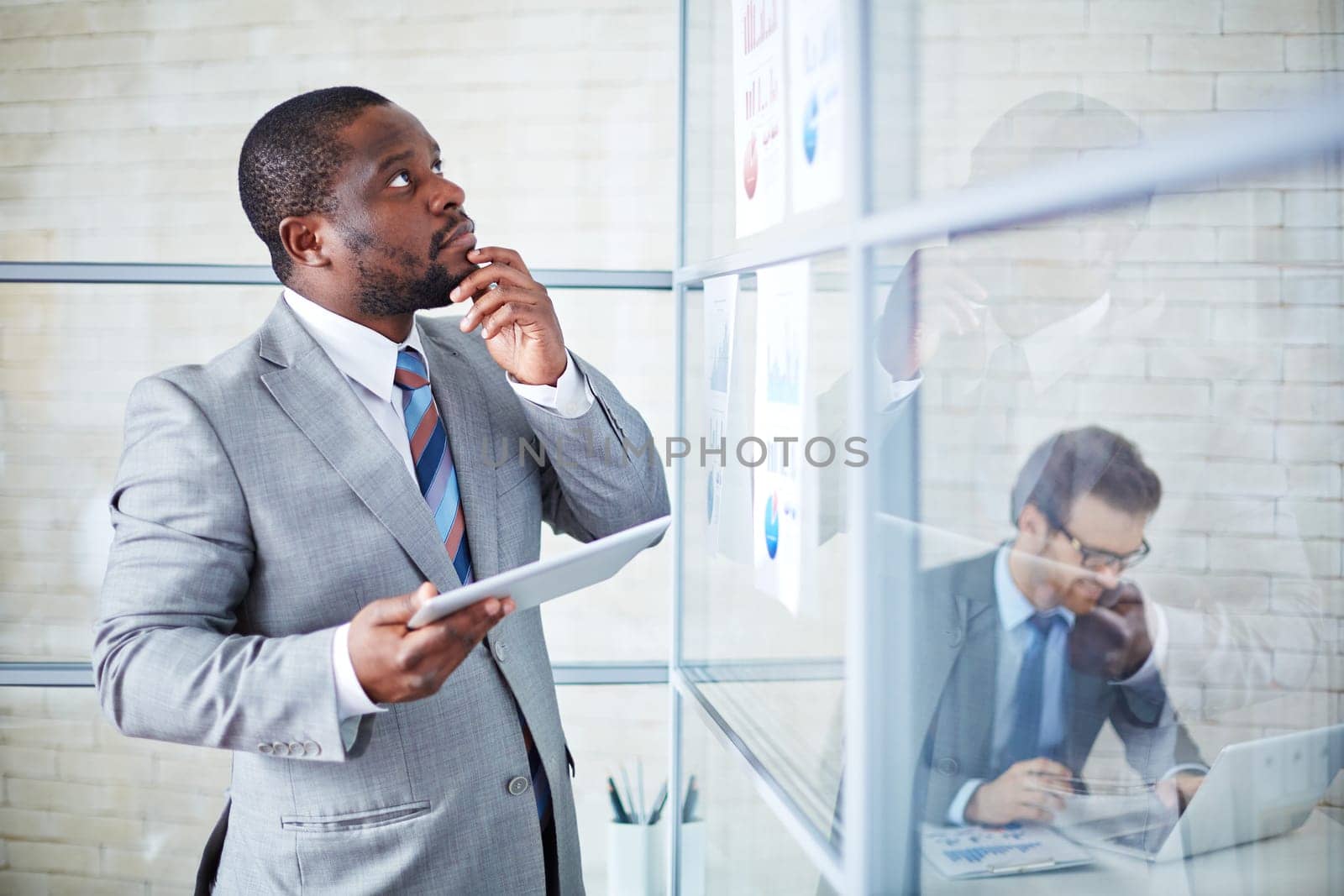Pensive businessman with touchpad looking at documents in office