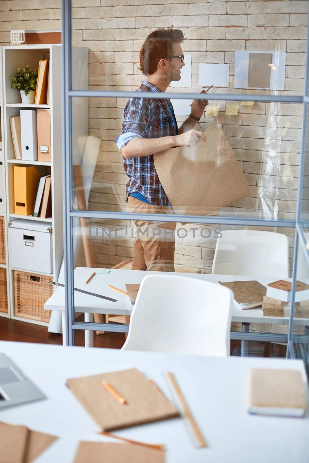 Young architect with blueprint reading papers on wall