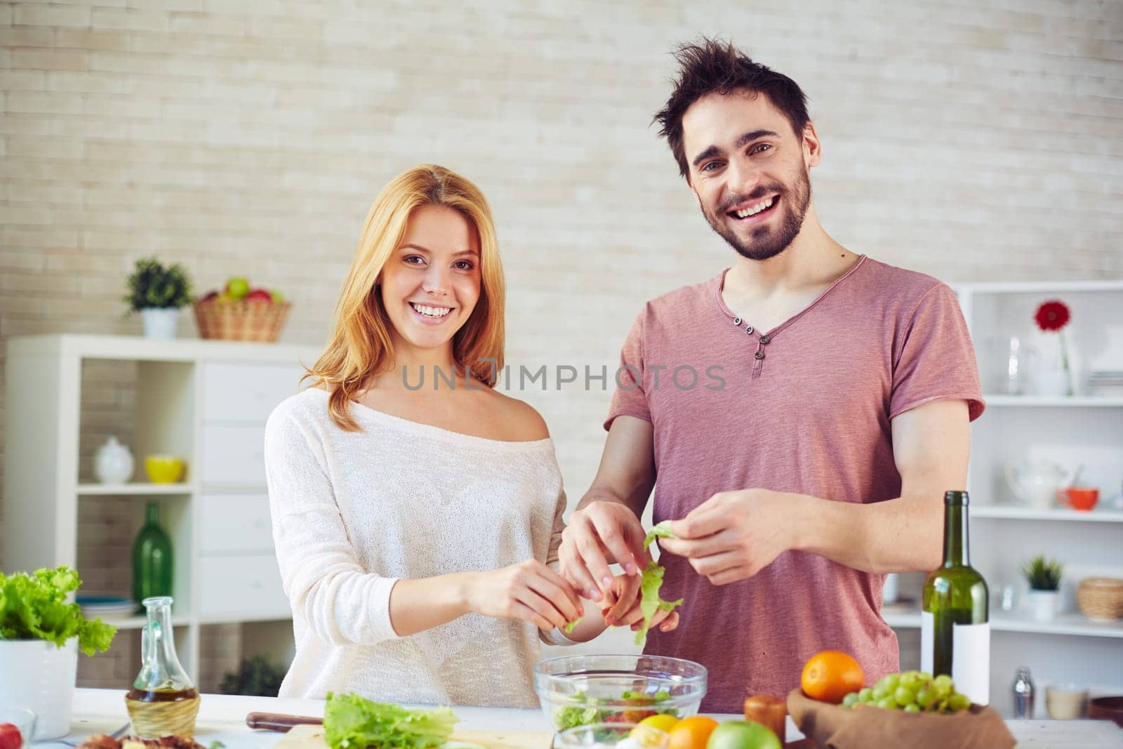 Amorous young couple looking at camera while cooking salad