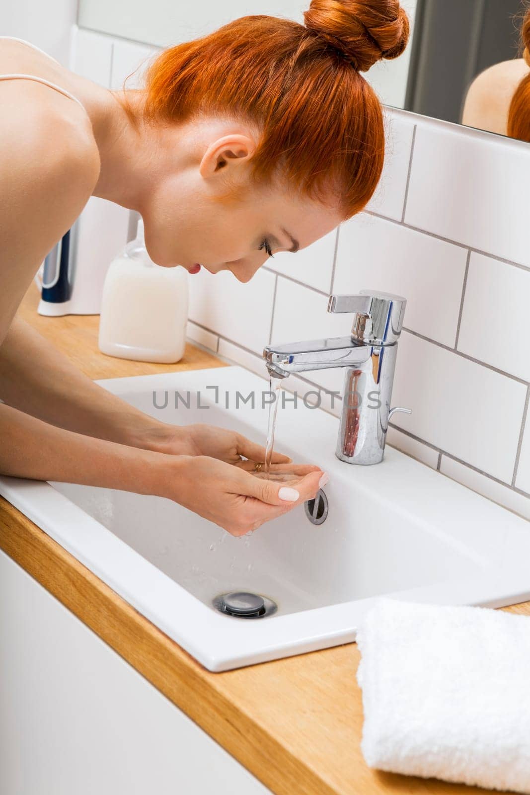Portrait of an attractive young woman with red hair in the morning in the bathroom while washing face skin care