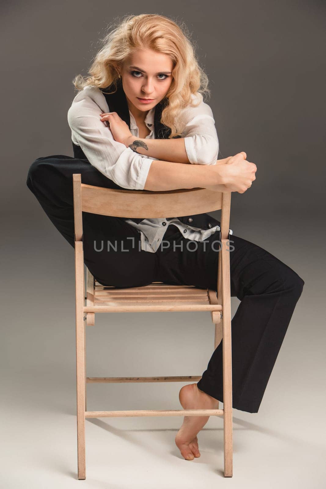Beauty blond woman  in a black suit and white shirt, sitting on a chair on a gray background
