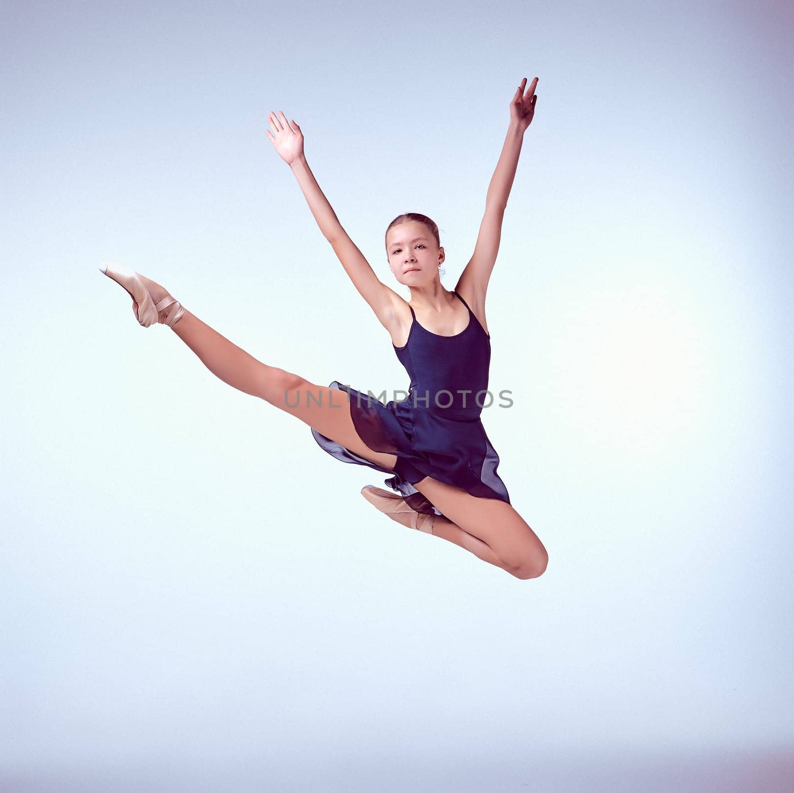 young ballet dancer jumping on a grey background. Ballerina is wearing in blue dress and pointe shoes