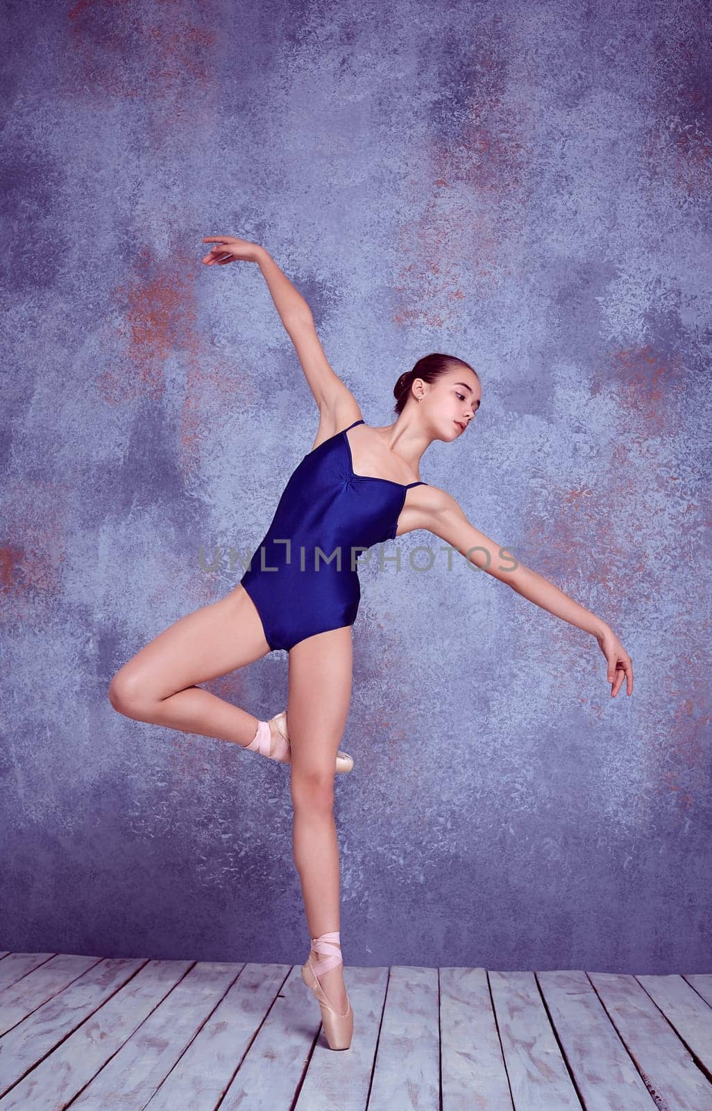 Young ballerina dancer showing her techniques on lilac background of wall and wooden floor