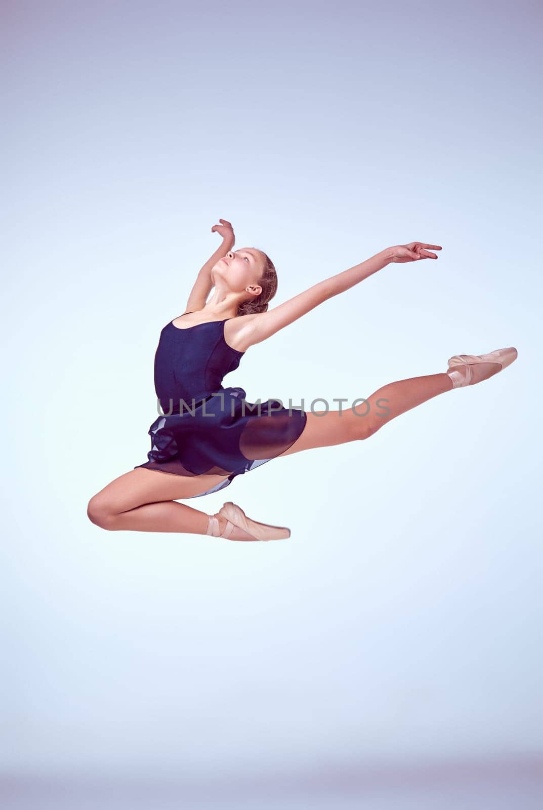 young ballet dancer jumping on a grey background. Ballerina is wearing in blue dress and pointe shoes