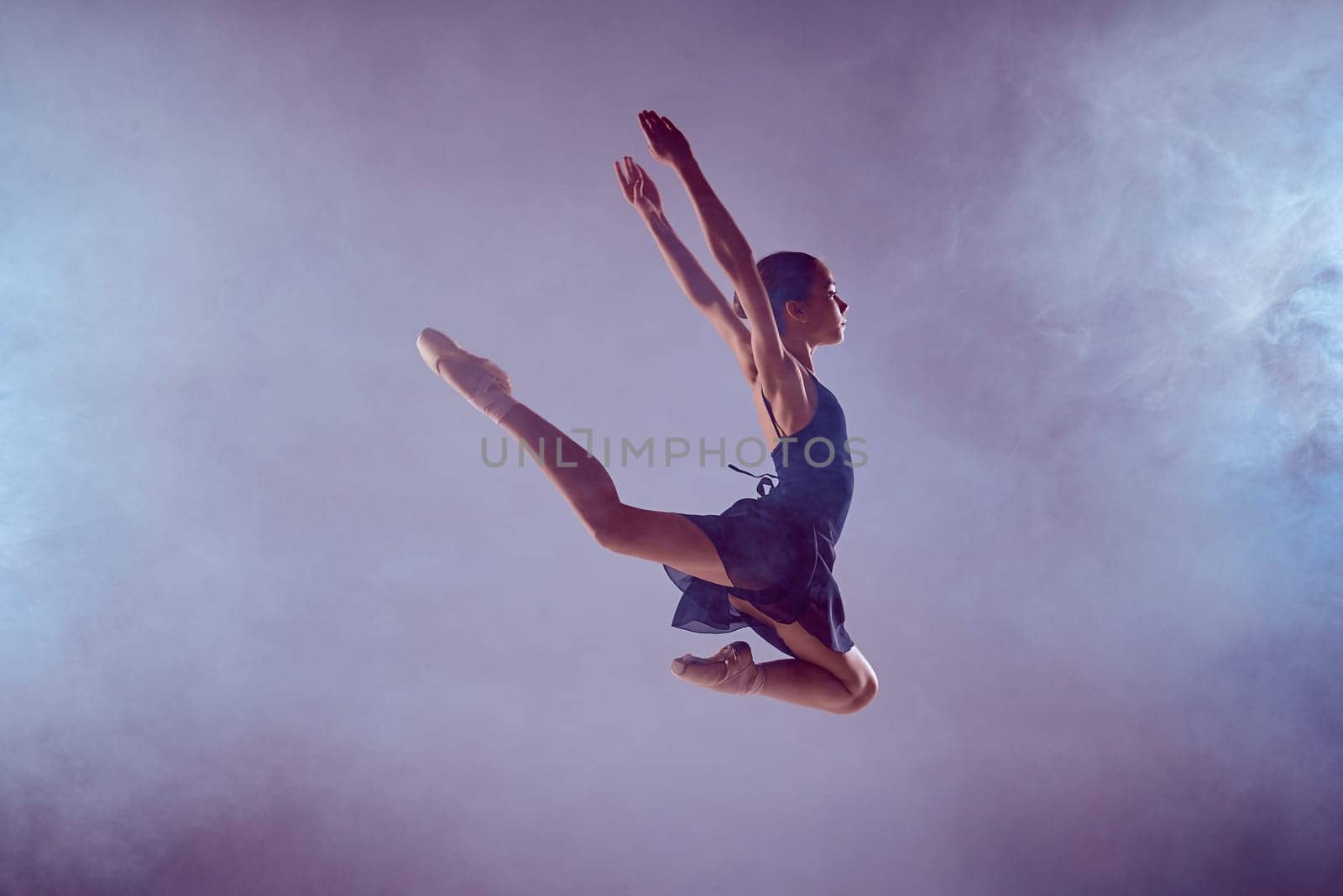young ballet dancer jumping on a lilac background. Ballerina is wearing in blue dress and pointe shoes. The outline shooting - silhouette of girl with smoke effect