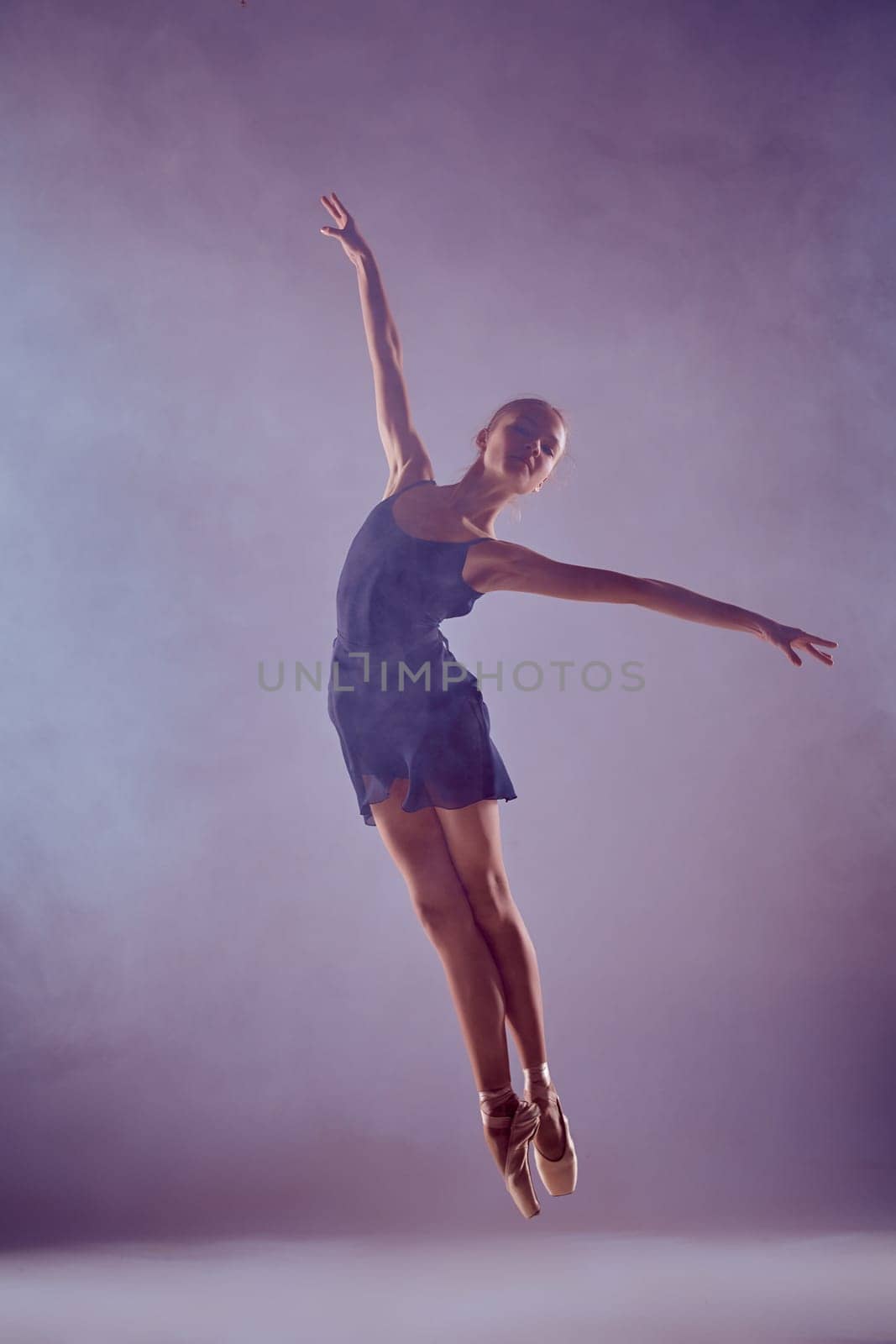 young ballet dancer jumping on a lilac background. Ballerina is wearing in blue dress and pointe shoes. The outline shooting - silhouette of girl with smoke effect