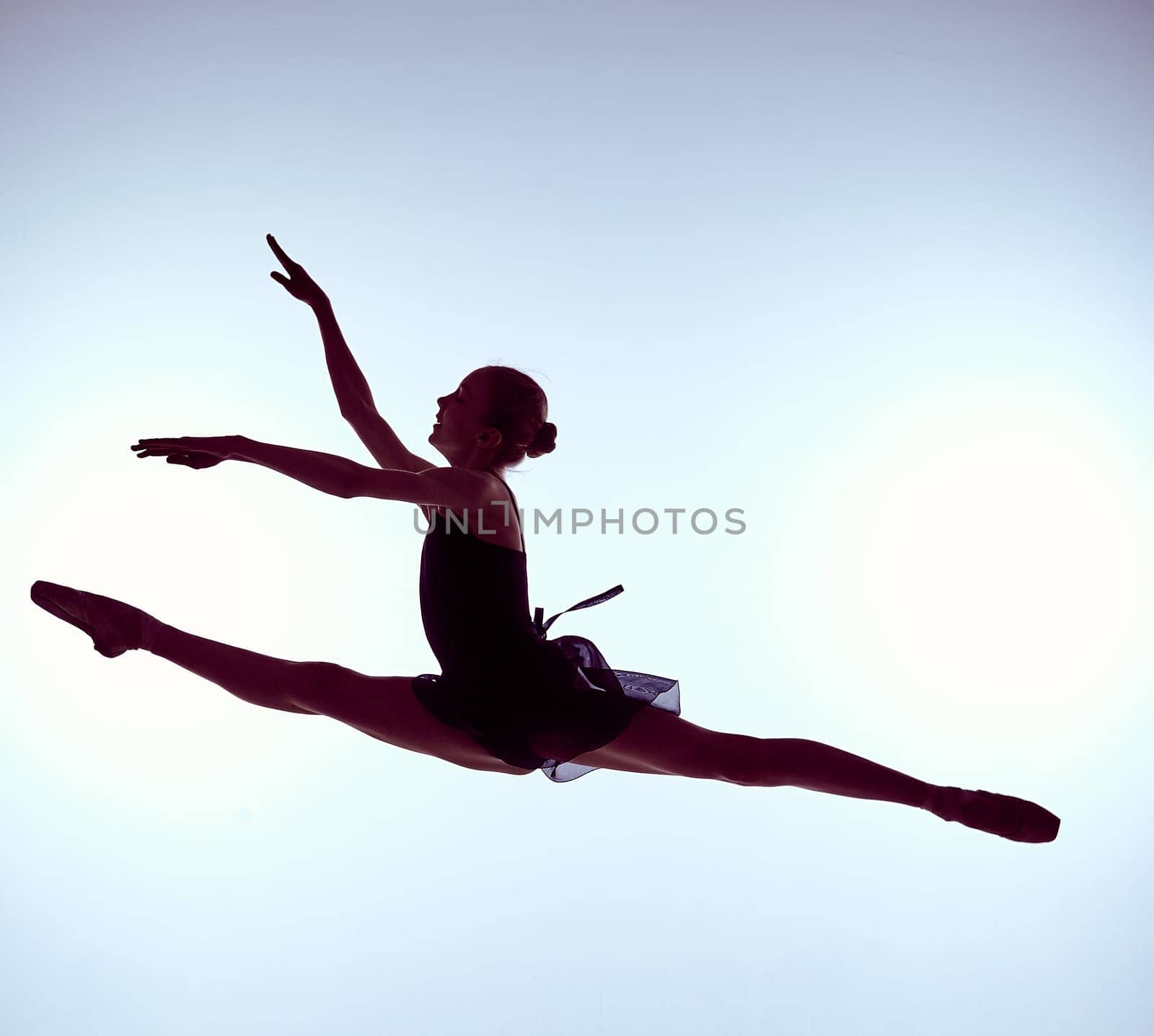 young ballet dancer jumping on a grey background. Ballerina is wearing in blue dress and pointe shoes. The outline shooting - silhouette of girl