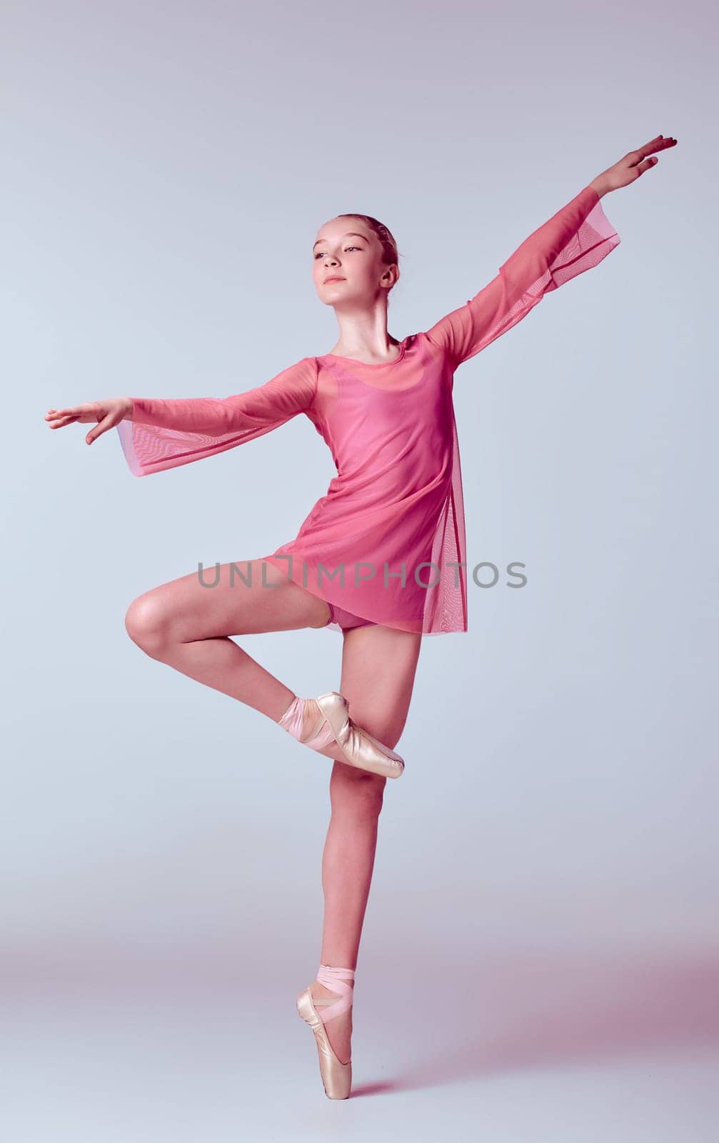 Young ballerina dancer in pink dress showing her techniques on lilac background