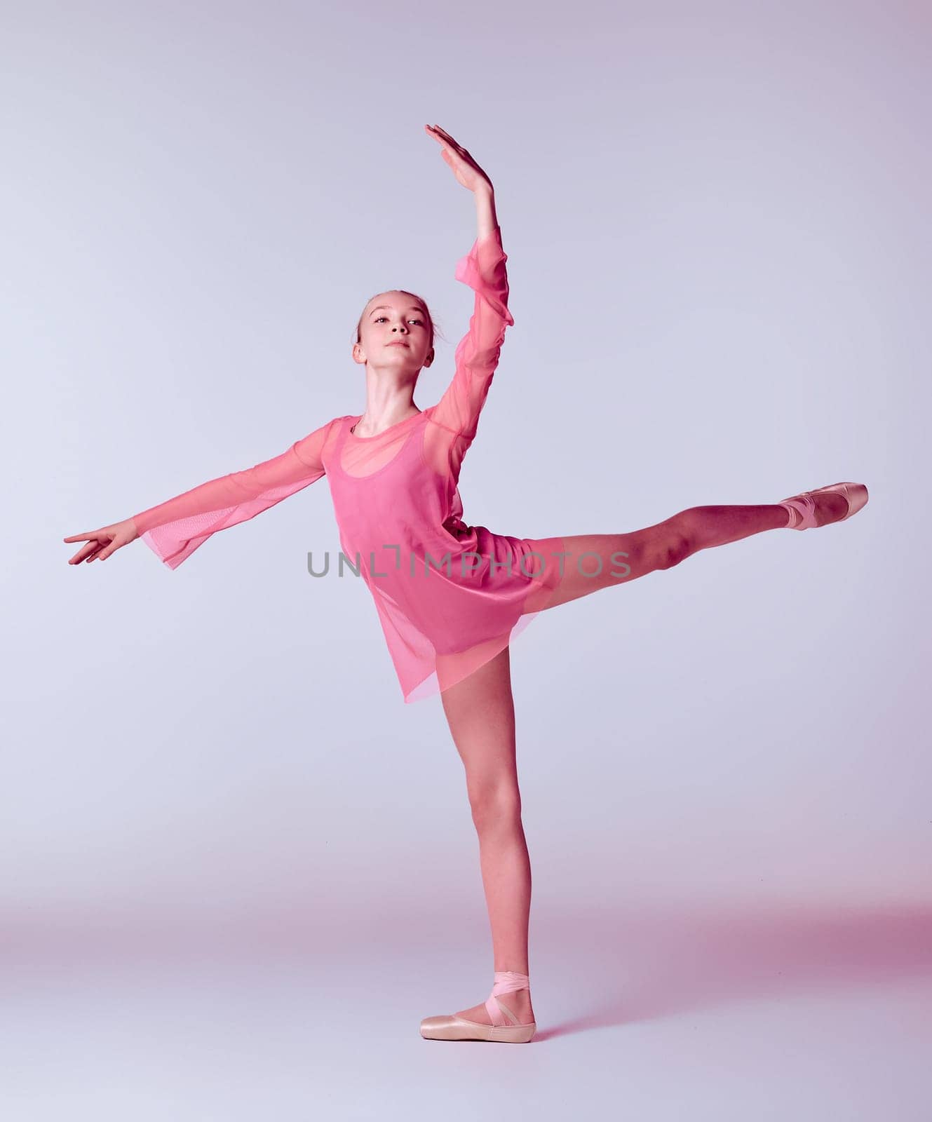 Young ballerina dancer in pink dress showing her techniques on lilac background