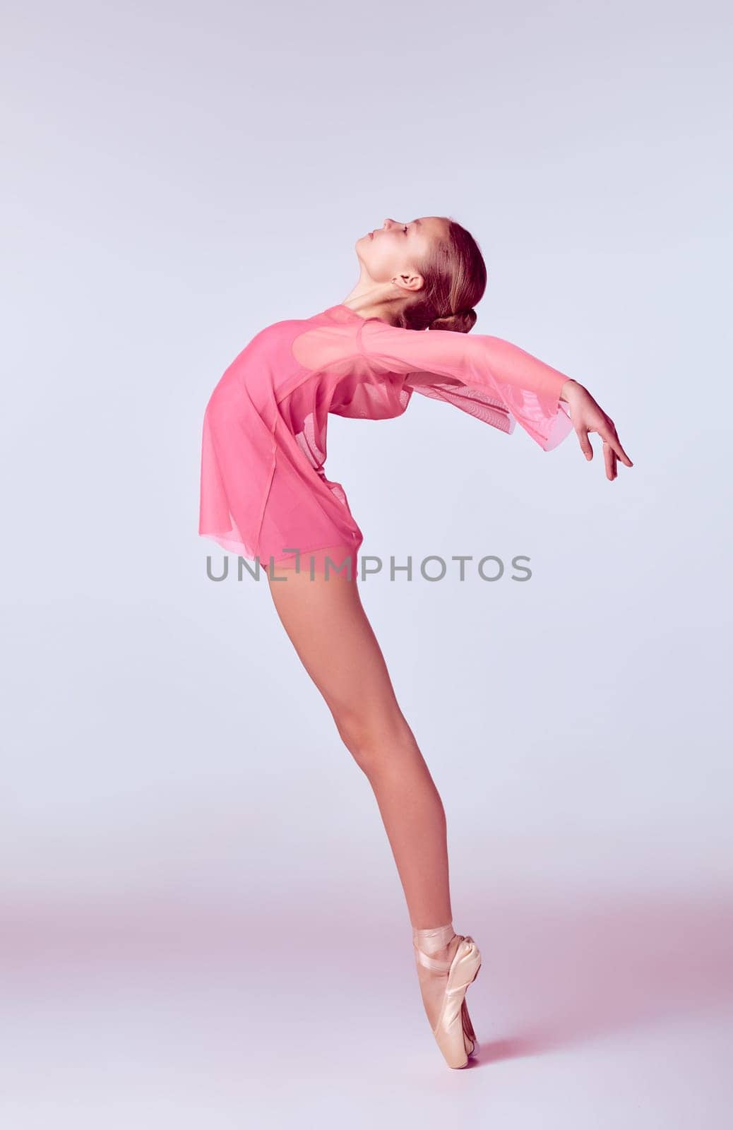 Young ballerina dancer in pink dress showing her techniques on lilac background