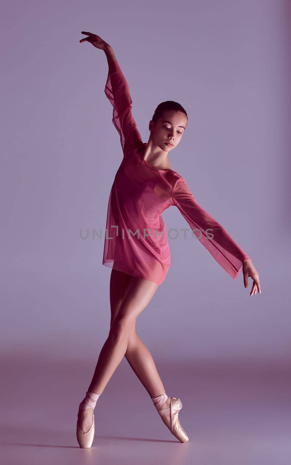 Young ballerina dancer in pink dress showing her techniques on lilac background