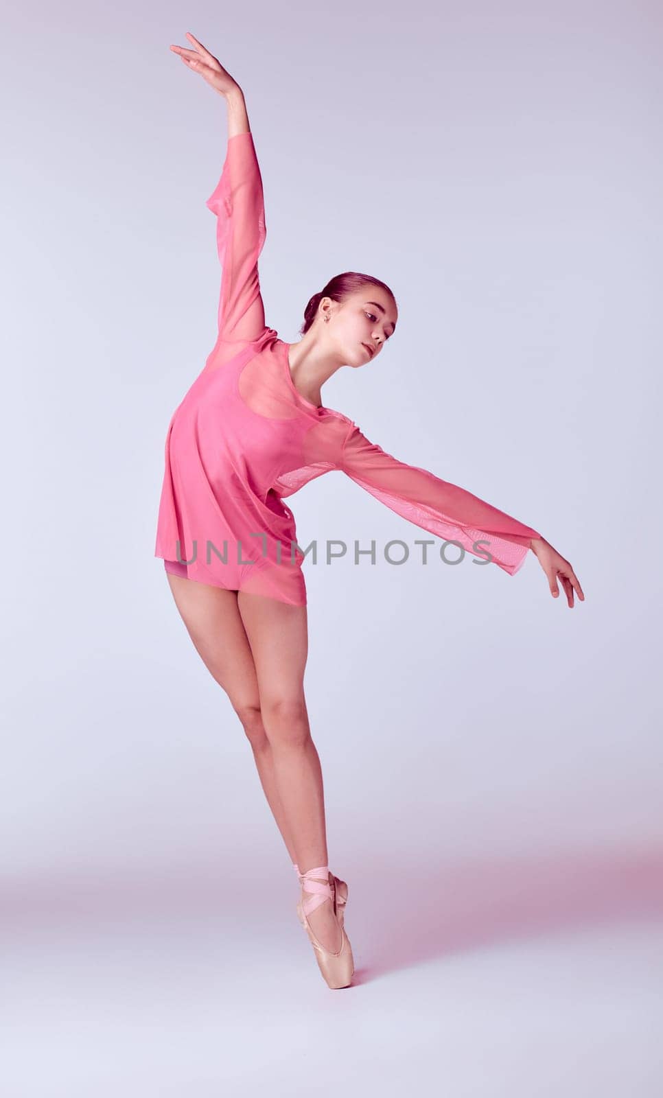 Young ballerina dancer in pink dress showing her techniques on gray background