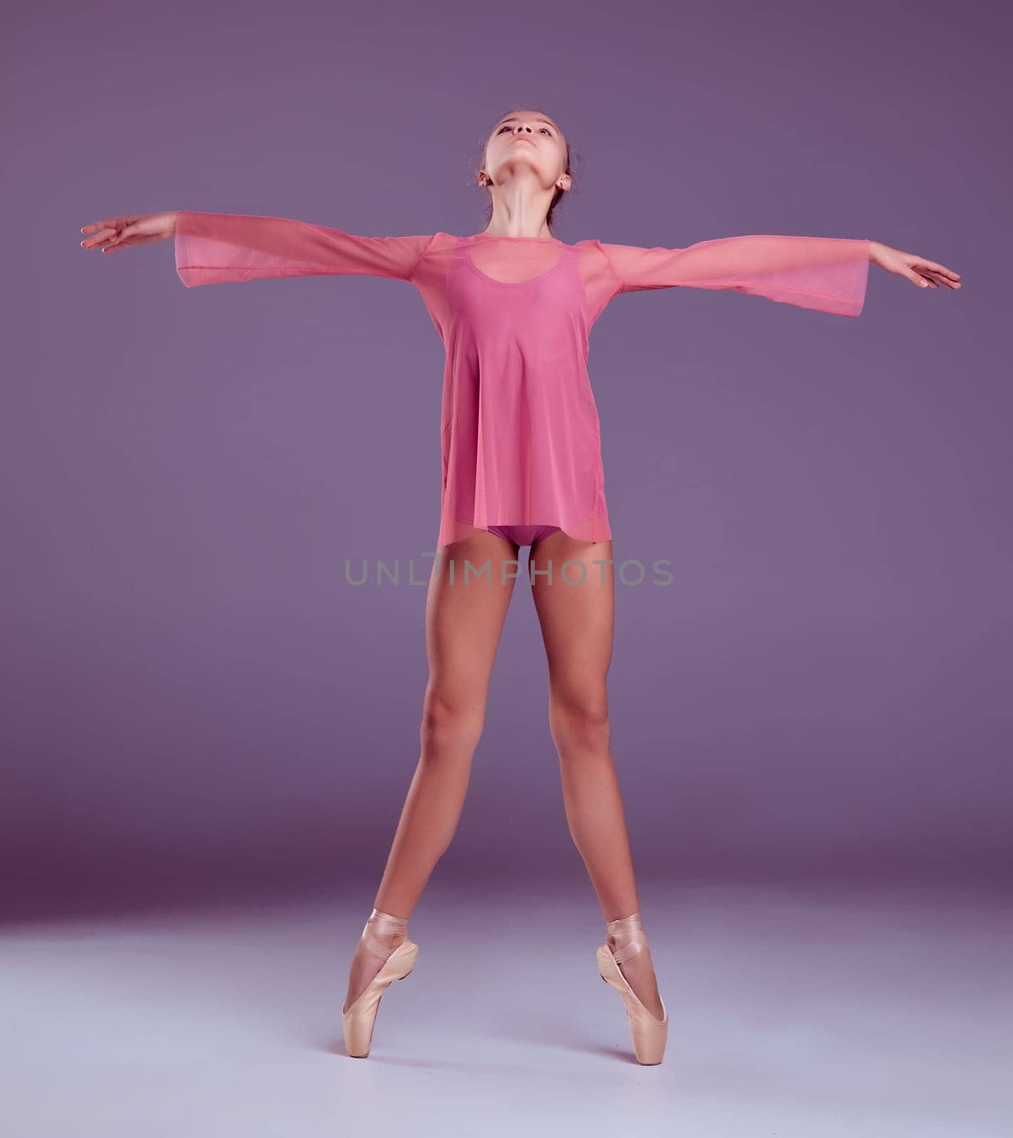 Young ballerina dancer in pink dress showing her techniques on lilac background